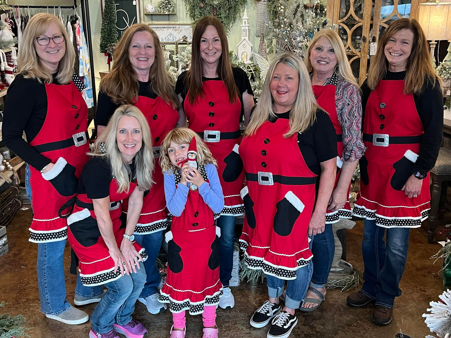 Group of women and a child wearing matching red aprons in a store setting.